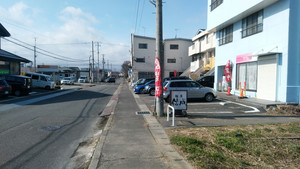 奥を横切る道路が「コスモス通り」。信成は、右手のビルの1階にある。