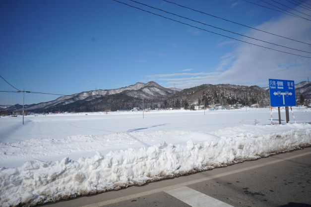 青い空に雪に埋もれた田畑、そこに迫る山並みが冬の終わりを待っている。